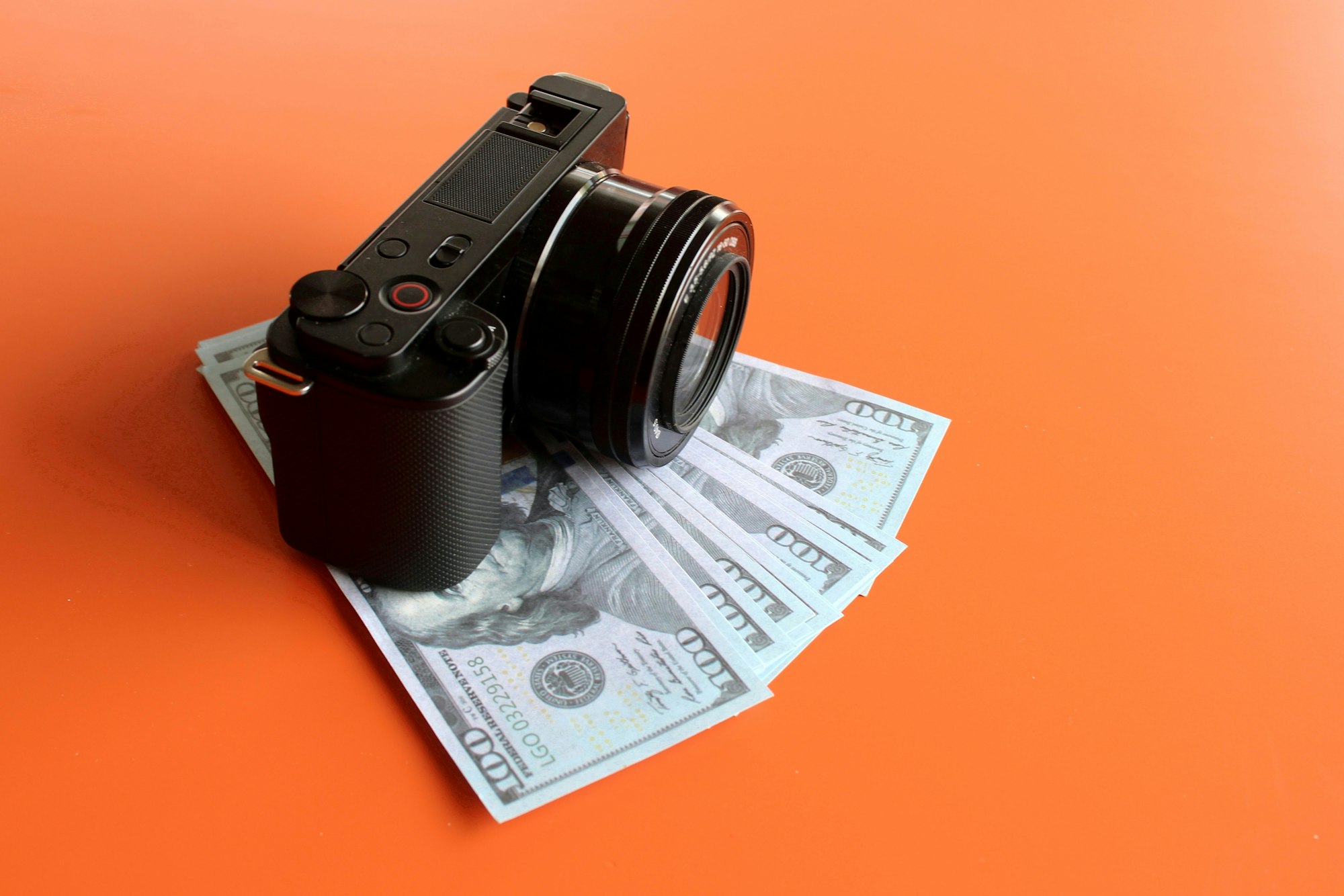 Mirrorless camera and money on orange background with copy space